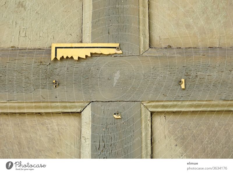 on a dilapidated wooden door you can see the remains of a yellow sign Wooden door Broken Crucifix broken Clue Illegible cross-headed screw Signage Warning sign