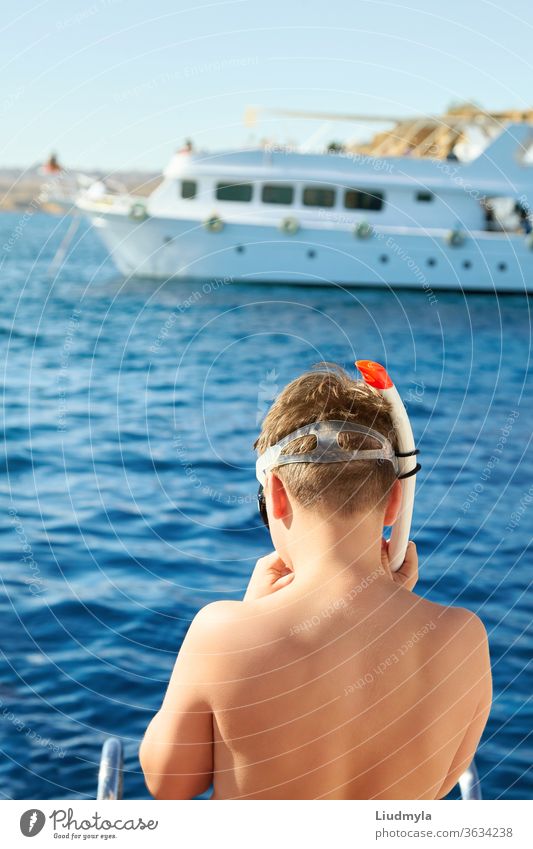 A boy is putting on a diving mask ready to swim in the sea. White yacht is on the background active beach blue child concept coral curious dive enjoyment