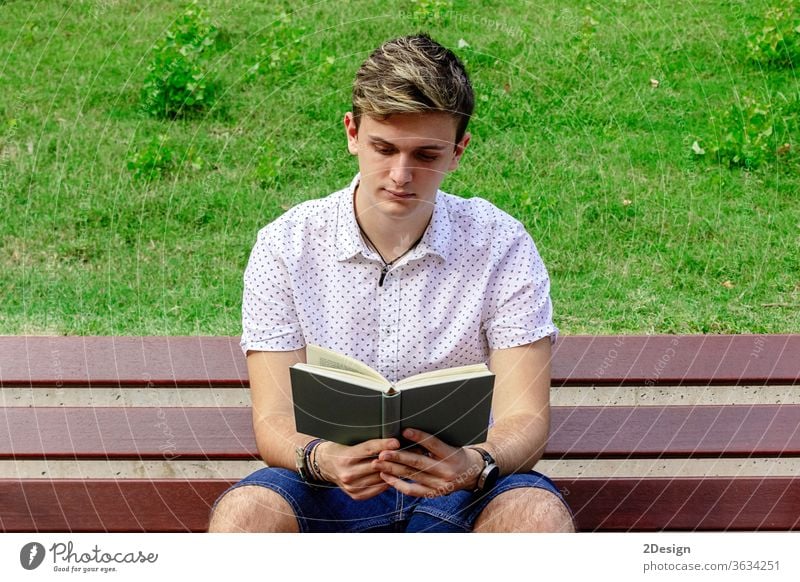Young man reading a book while sitting on a bench in a park male young 1 photogenic adult person summer student caucasian leisure smiling nature casual attire