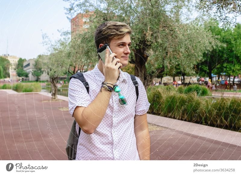 Young man using mobile phone while walking outdoors holding young 1 happy face person cool casual attire calling hispanic one person conversation adult modern