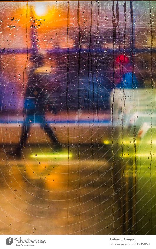 Window with raindrops and city lights with one person in the background closeup texture unrecognizable silhouettes move impressionism lifestyle windshield urban
