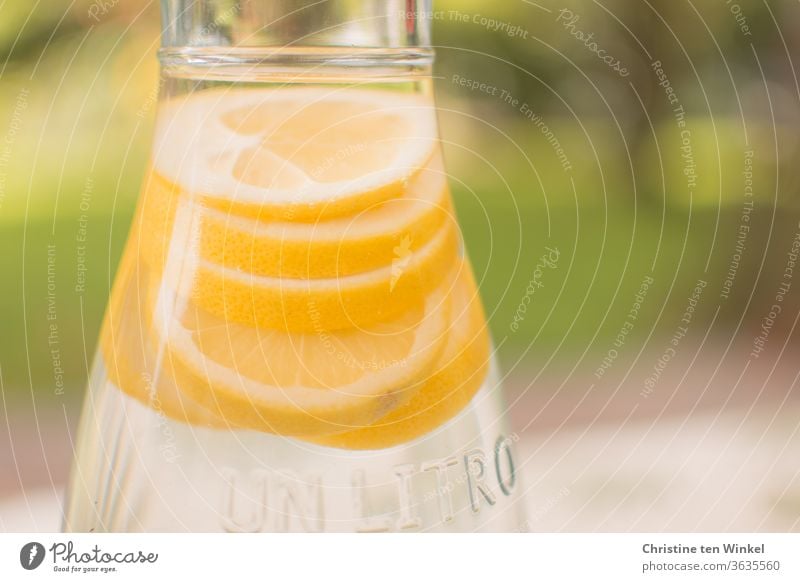 bright yellow slices of lemon in a carafe filled with water. Weak depth of field, green areas in the background Lemon slices water carafe Water Drinking water