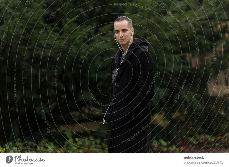 Young Man Listening to Earphones in Park with Thinking Facial Expression man portrait earphones listenings caucasian ethnicity outdoors medium shot