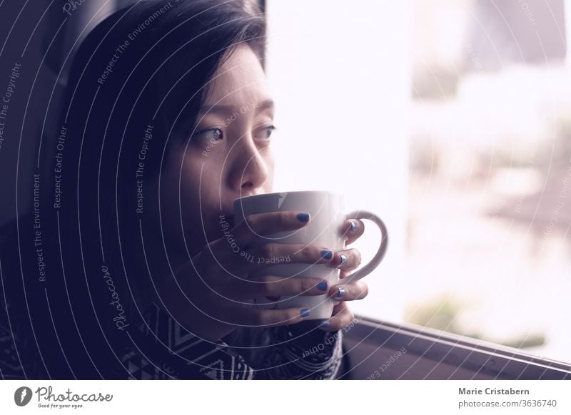 Asian girl having coffee on an early autumn morning beside the window, shows concept of new normal, home quarantine and self isolation during covid-19 pandemic