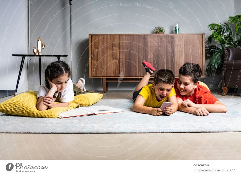 Little girl reading a book while two boys playing with a smart phone brothers cell phone cheerful child childhood children communication cute data different