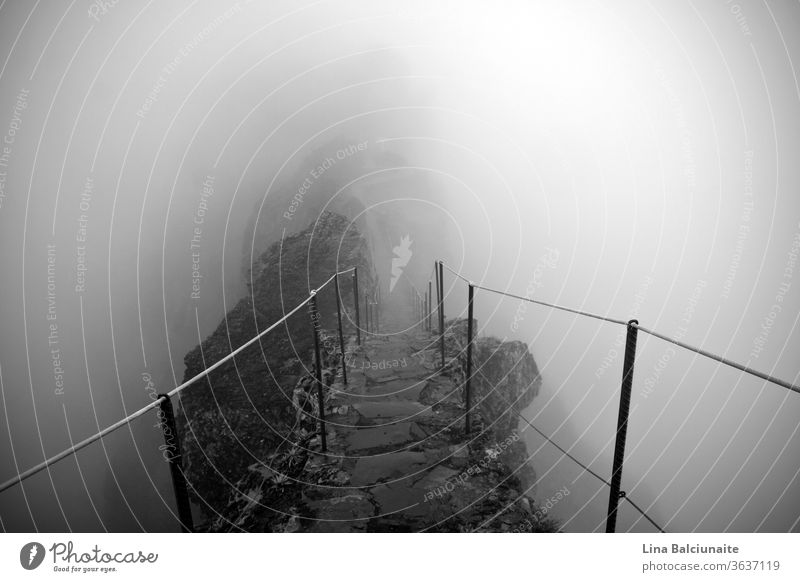 Black and white photo of the way to the mountain peaks Pico Ruivo and Pico do Areeiro in the fog in Madeira, Portugal. A mystical path, way to nowhere Above