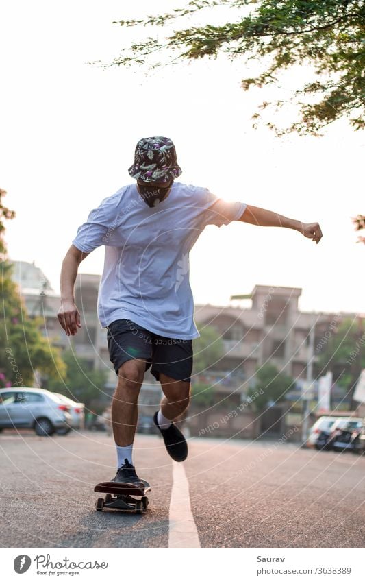 Front view of a young adult skateboarding on an empty street while wearing a protective mask during sunrise. summer recreation covid-19 new normal outdoors