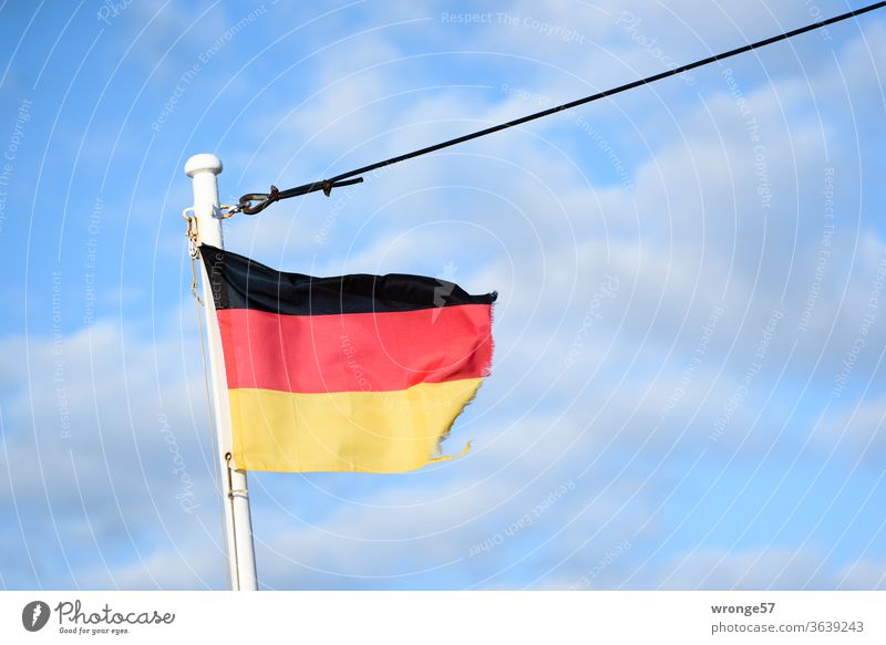 Frayed German flag fluttering in the wind on the mast of a ship under a blue sky Flag Germany German Flag Pole Bowmast Flagpole black red gold black-red-gold