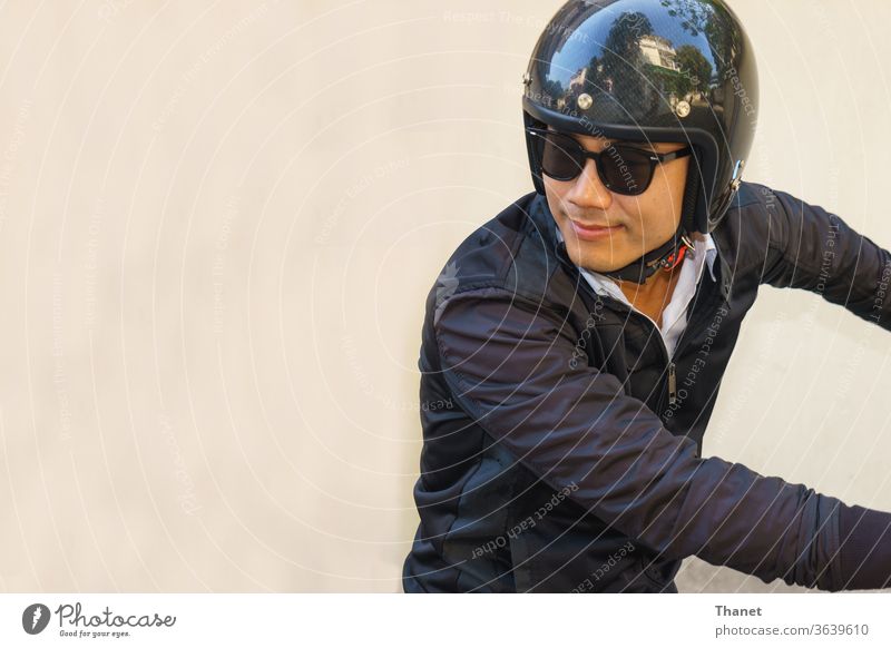 Young Asian motorcyclist wearing black jacket is looking back while riding his motorcycle. asian biker handsome helmet man motorbike rider sunglasses young