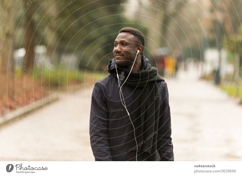 Young Black Man with Earphones Looking Away and Walking in Park portrait earphones man African ethnicity black public park listening music audiobook