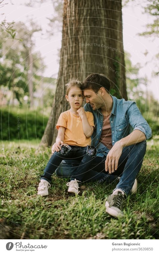 Single father sitting on grass by the tree with little daughter nature girl happy man park people family parent child kid love dad fun adult childhood summer