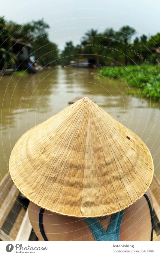 Woman in a boat with a rice hat in Vietnam conical cap Non La River voyage Mekong Mekong Delta Yellow traditionally Straw Rice Straw Driving Water Brown green