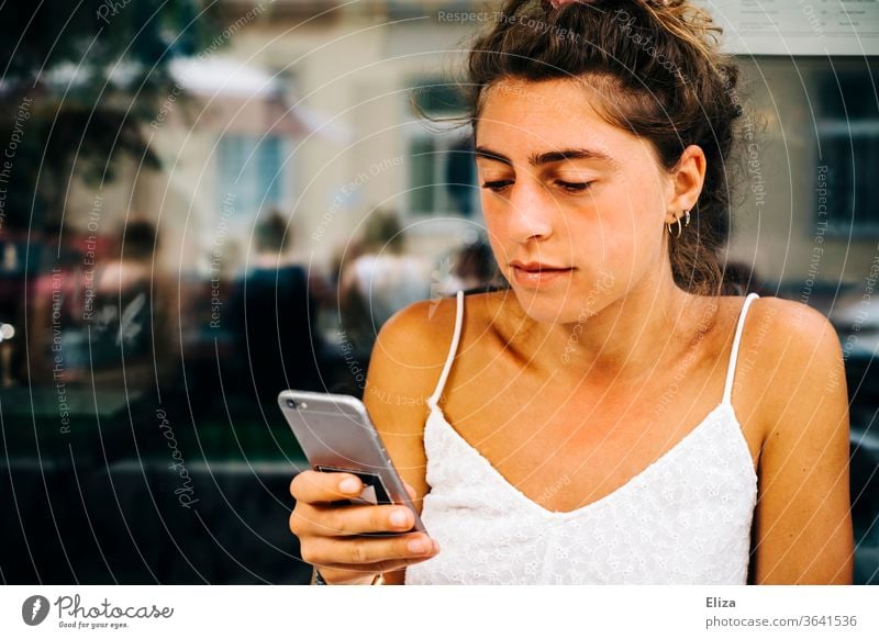 Young woman sitting outside in a café looking at her smartphone Sun mobile Reading employed Telephone girl concentrated Lifestyle Summer Summery already