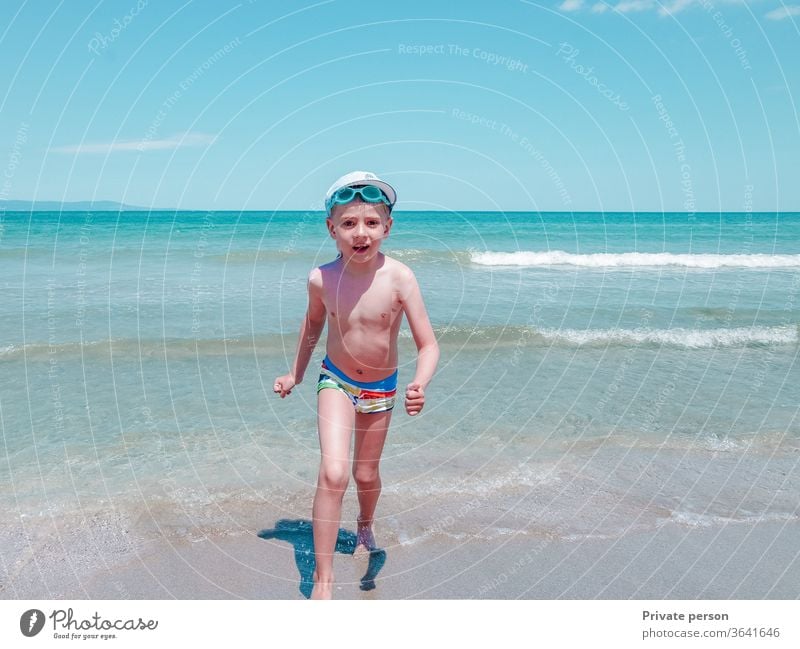 Happy little smiling boy runs along the seashore on a sunny summer day happy small beach sky blue young lifestyle sand outdoors beautiful cute one pretty hat