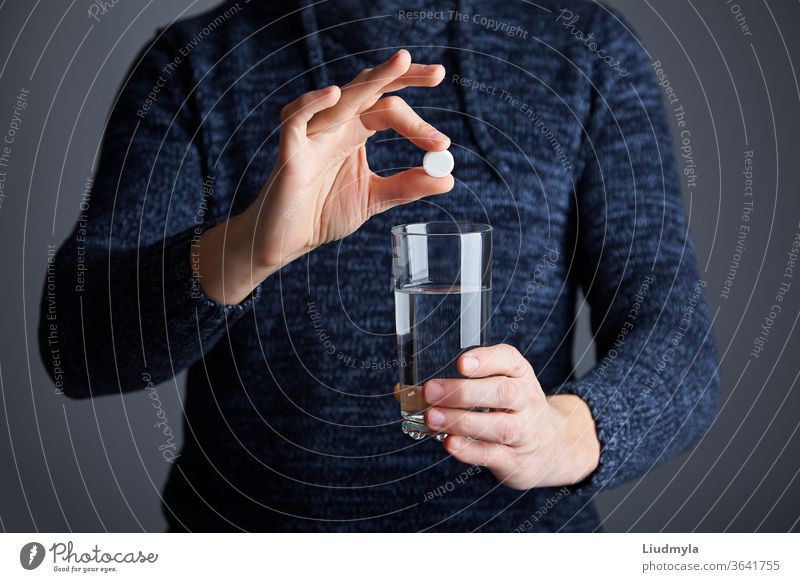 Male ready to dissolve the pill in water. Soluble white pill and a glass of water in his hands. Effervescent tablet aspirin in glass of water business young