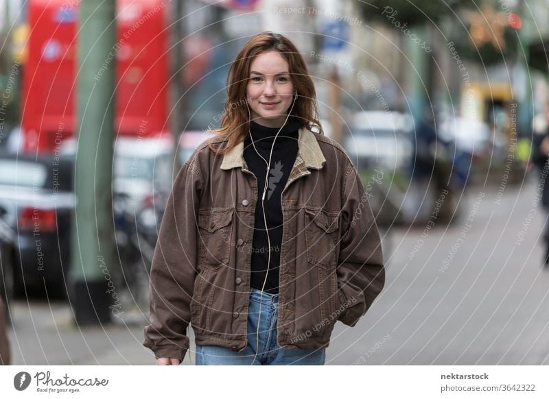 Happy Young Woman Listening to Earphones on Sidewalk caucasian ethnicity woman female earphones audio music listening sidewalk street casual clothing smile