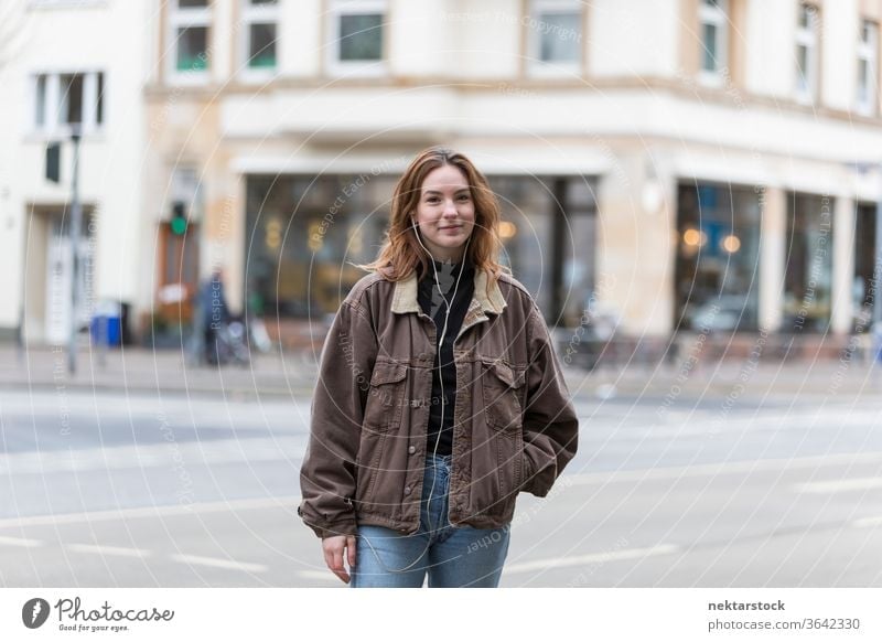 Young Woman with Genuine Smile Standing on City Street caucasian ethnicity woman female earphones audio music listening sidewalk street casual clothing smile