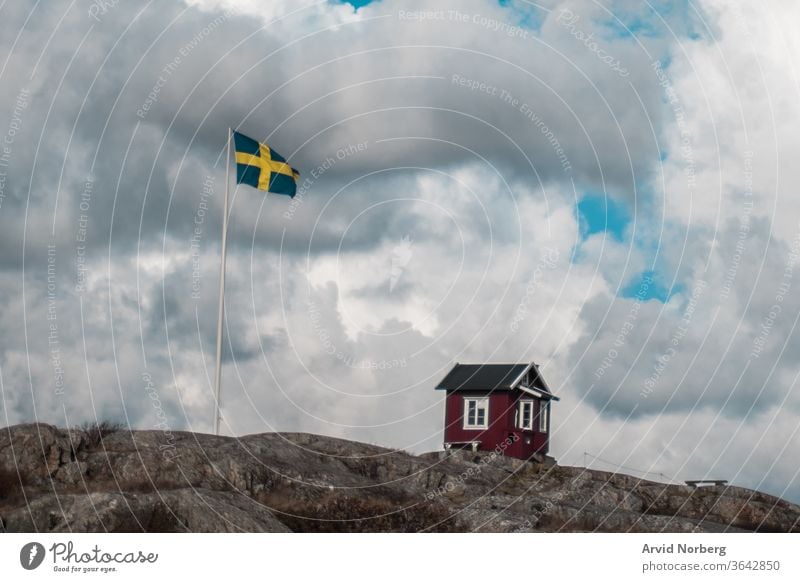 A traditional red and white small hut next to Swedish flag in Gothenburg southern archipelago, Sweden baltic beautiful beauty black blue cloud clouds coast