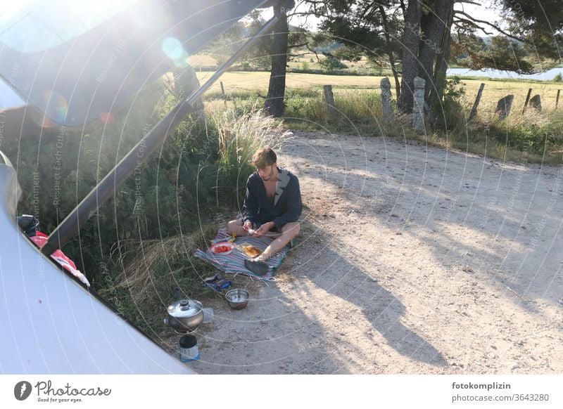 young man sits on a dirt road and prepares a picnic break on the road again Young man Picnic Vacation & Travel In transit off off the beaten track Freedom