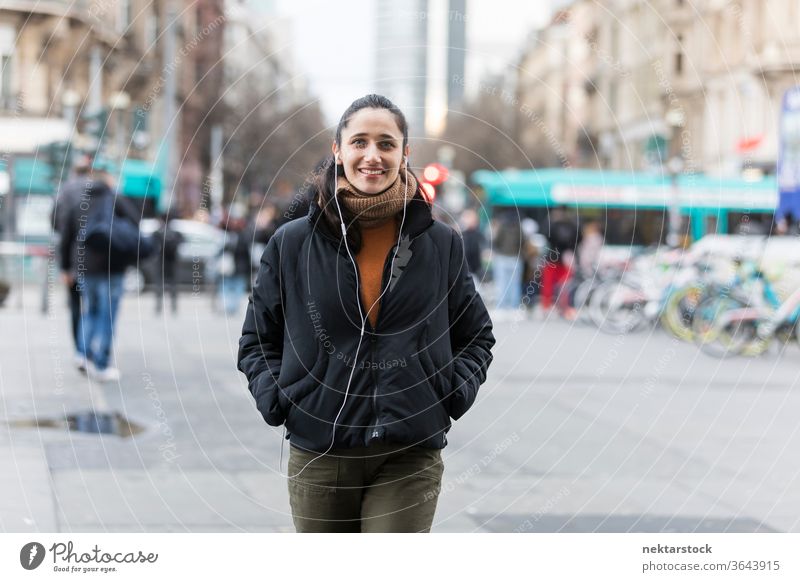 Young Indian woman walking on street listening to earphones and smiling at camera. young woman Indian ethnicity music medium shot audiobook focus on foreground