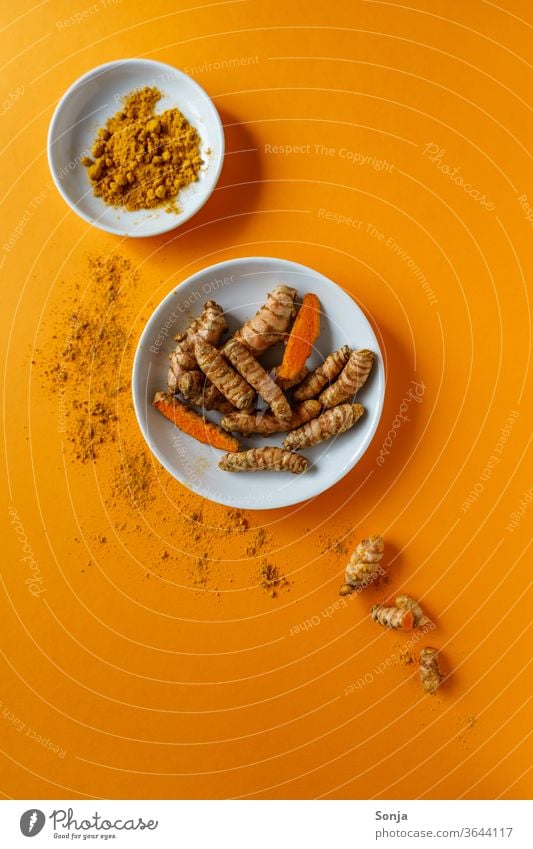 Turmeric roots in a bowl and powder on an orange background. Top view, healthy food. turmeric Root Yellow Curcuma Herbs and spices Colour photo Orange