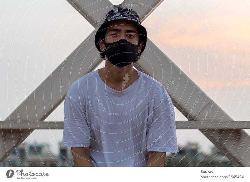 A young male put a protective face mask on to avoid Corona Virus infection in a city while wearing a floral bucket cap and a white t-shirt.. coronavirus