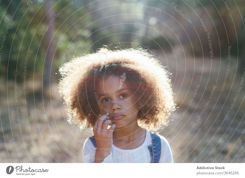 Serious little mulatto girl on blurred nature background black child serious portrait calm adorable summer style outfit unemotional curly hair cute sunlight