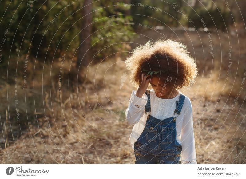 Serious little mulatto girl on blurred nature background black child portrait calm adorable summer style outfit unemotional curly hair cute sunlight sunny stand