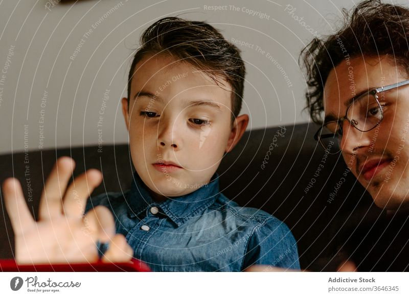 Schoolboy with brother browsing tablet on comfy sofa siblings using gadget contemporary relax rest chat legs crossed surfing connection cozy together point