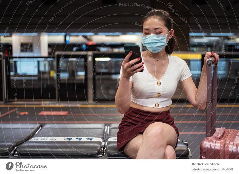 Asian woman in mask using smartphone in airport rail link suitcase train station travel respirator coronavirus covid 19 browsing epidemic cellphone passenger