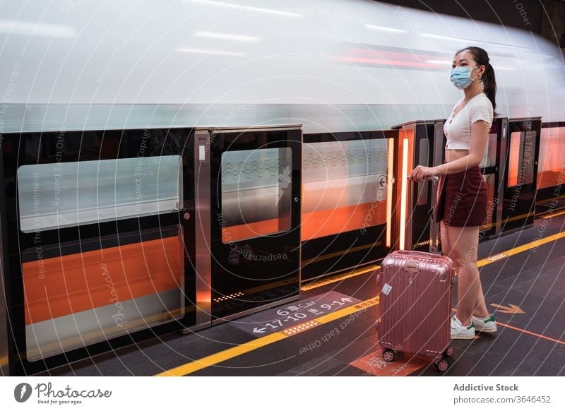 Asian woman in respirator waiting to board train in station railway station suitcase travel platform coronavirus calm cabin passenger covid 19 epidemic mask
