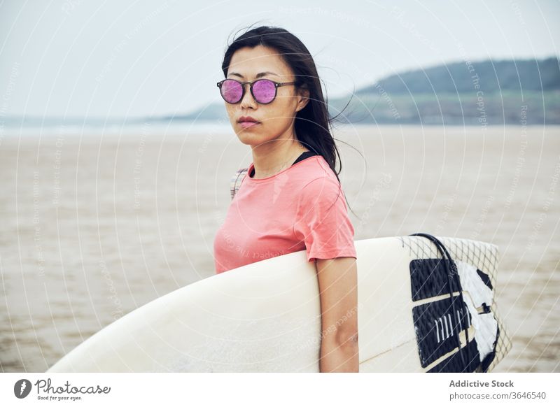 Content female surfer walking on beach with surfboard woman sandy carry content sea casual seaside carefree activity young sporty tranquil lifestyle sunglasses