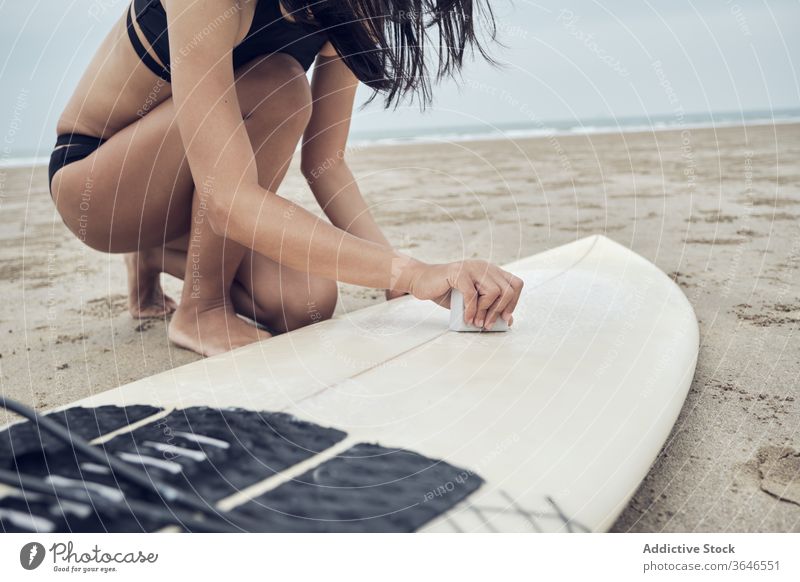 Crop female surfer waxing surfboard with basecoat woman prepare beach sandy sporty sea swimwear activity seaside carefree tranquil lifestyle sunglasses seashore