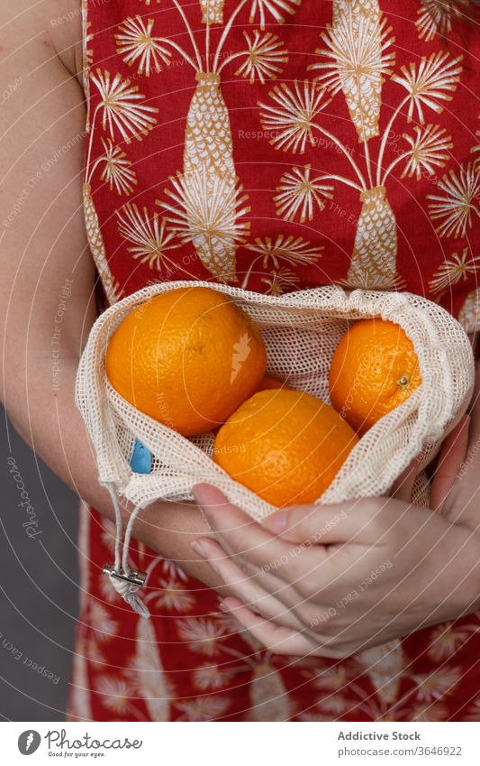 Crop woman with fresh fruits in string bag ripe orange shopping bag reuse eco friendly healthy food female ecology summer purchase grocery stand shopper