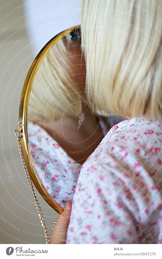 At home, in a bright apartment, blonde girl holds a golden mirror in her hand and looks at it, curiously identifying her reflection. Childlike, playful self-observation, perception. Blue eye of a child in a mirror with a golden frame. Two.