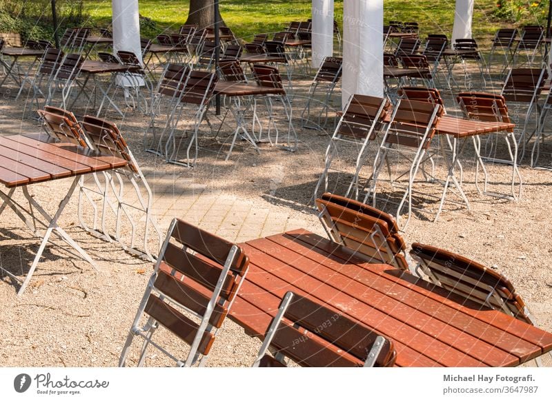 empty chairs and tables folded up in a beer garden Corona crisis rules of conduct ban on going out social distance restaurant parasols wooden chair