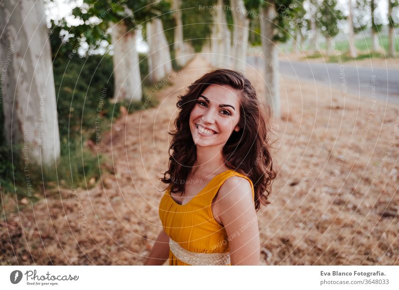 portrait of young beautiful woman wearing a yellow dress standing in a path of trees. Summertime and lifestyle adventure back beauty bright brunette casual