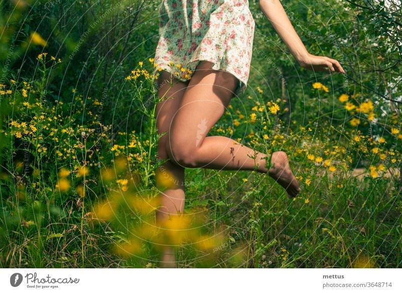 Happy girl dancing in the summer grass and yellow wildflowers legs dance part of body dress jump active female young beauty beautiful people action adult nature
