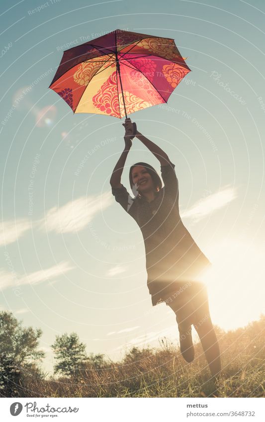 A young body-positive girl dances with a colored umbrella in a meadow illuminated by the sun at sunset. female freedom happy dress emotion classic person image