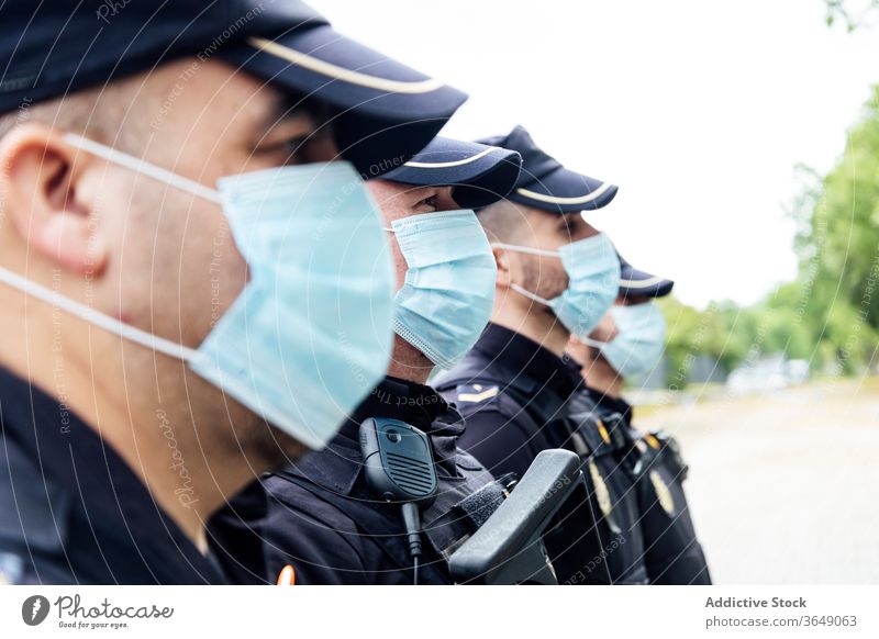 Policemen in medical masks standing on street against service vans patrol police protect control serious safety work professional secure squad uniform gun