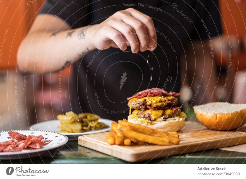 Crop male cook sprinkling salt on burger add man prepare tasty delicious cutlet cafe table chef lunch meal professional food work sprinkle yummy guy cafeteria