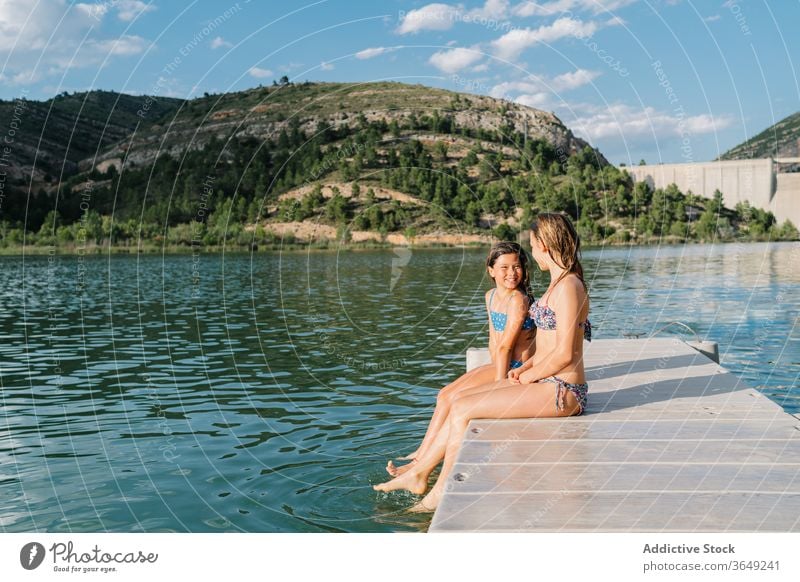 Carefree sisters resting on pier in summer vacation swimwear bikini girl lake quay cheerful together childhood smile friendship relax sit joy weekend