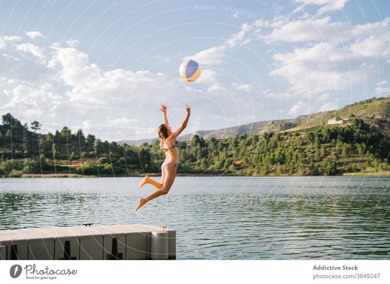 Playful teenage girl jumping in lake from pier beach ball play pond summer holiday vacation enjoy inflatable rubber bikini water relax nature playful summertime