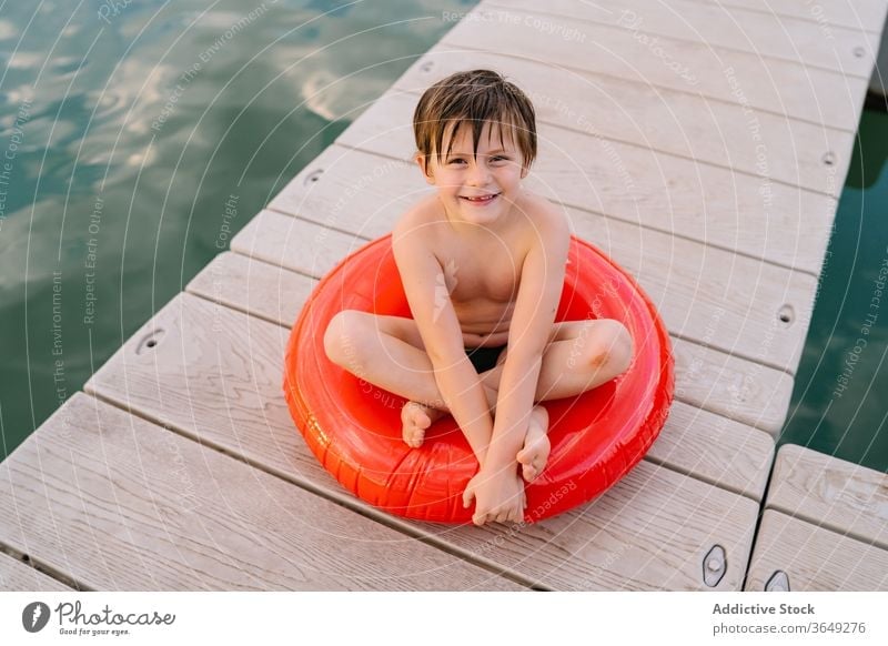 Carefree boy on rubber ring on quay lake pier child relax holiday carefree smile inflatable preteen adorable water wooden summer vacation kid childhood rest joy