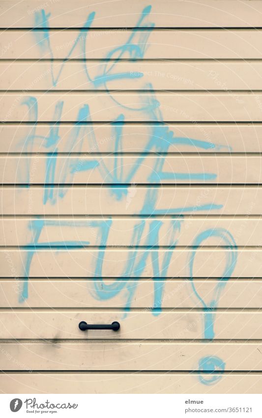 "WE HAVE FUN" is written in large light blue graffiti on a beige metal garage door above the handle we have fun Daub Graffiti Garage door Damage to property