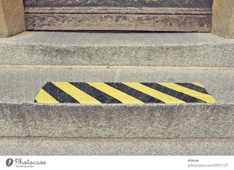 yellow-black signal strip as spacer on a stair step in front of an old wooden door gap protective measure Contact ban Protection against infection corona