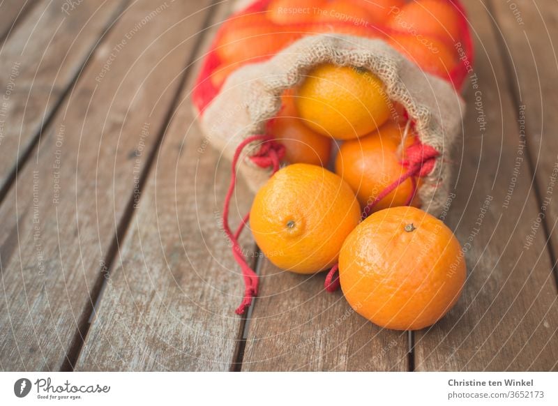 An opened bag of mandarins lies on an older wooden table. Two fruits lie in front of the bag. Close-up with shallow depth of field Citrus fruits Fresh