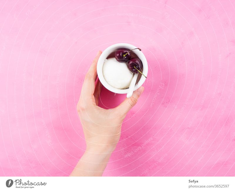 Frozen yogurt dessert in cup in female hand scoop sorbet holding gelato ice cream pink cherry minimal frozen white berries sundae sweet fruit fresh temptation