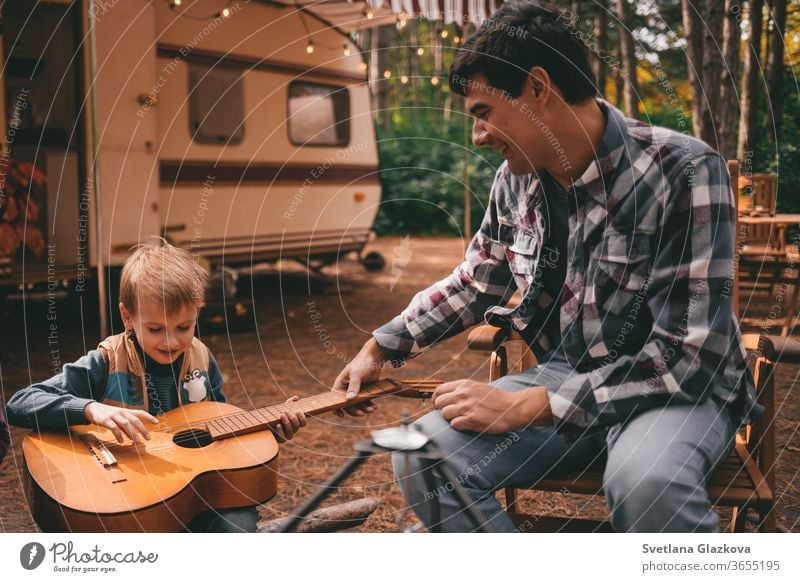 Father teaches son play guitar on camping trip relaxing in the autumn forest. Camper trailer. Fall season outdoors trip family fall nature father mother