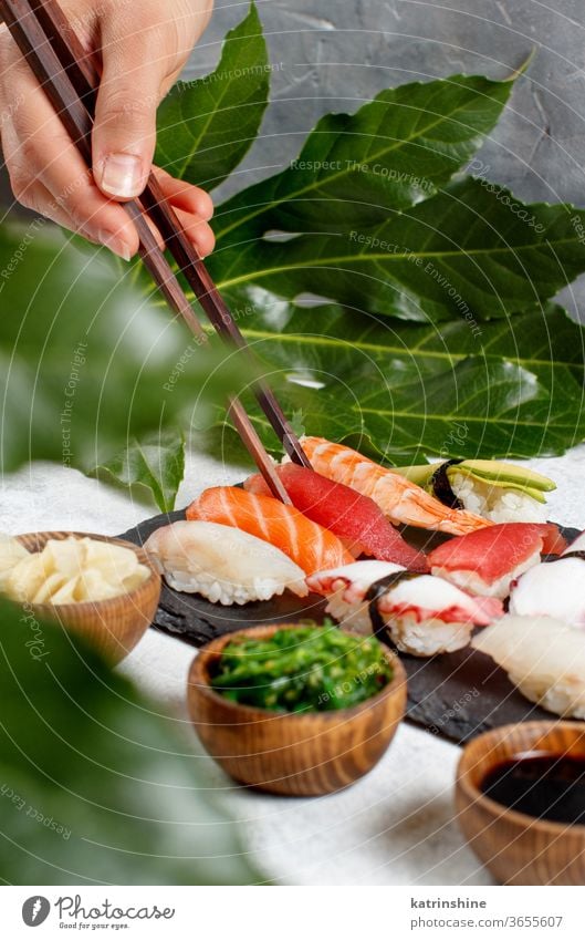 Close up of hand taking suchi with chopsticks from a plate sushi ready to eat eating Sashimi Rolls sushi bar leaf copy space dinning Japanese Culture Seafood